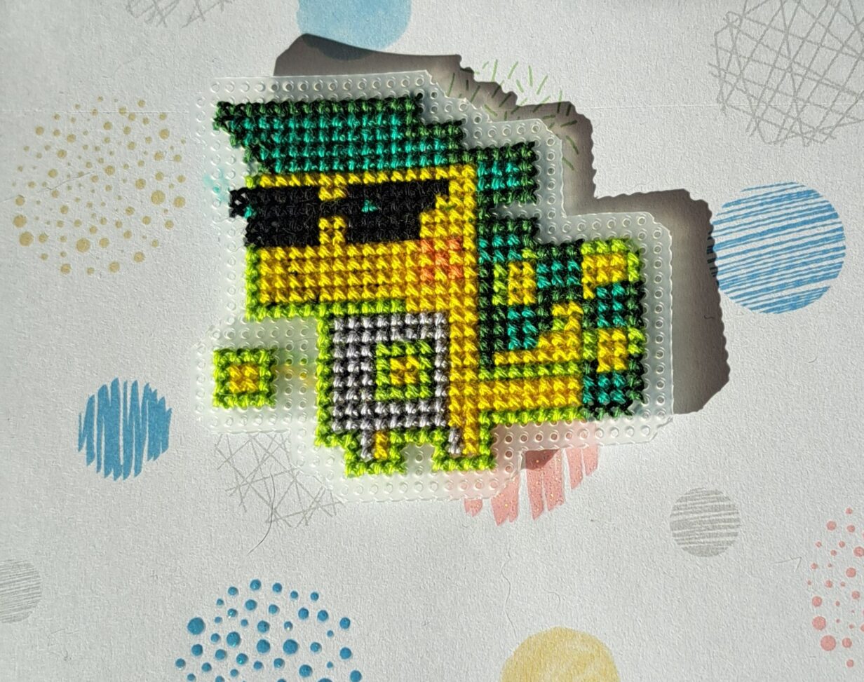 Ajaw brodé. Personnage reptilien vert et jaune avec des lunette de soleil cool.